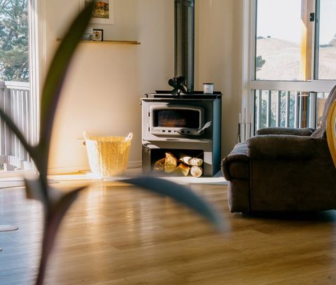 The wood stove in golden afternoon light, logs stacked and ready